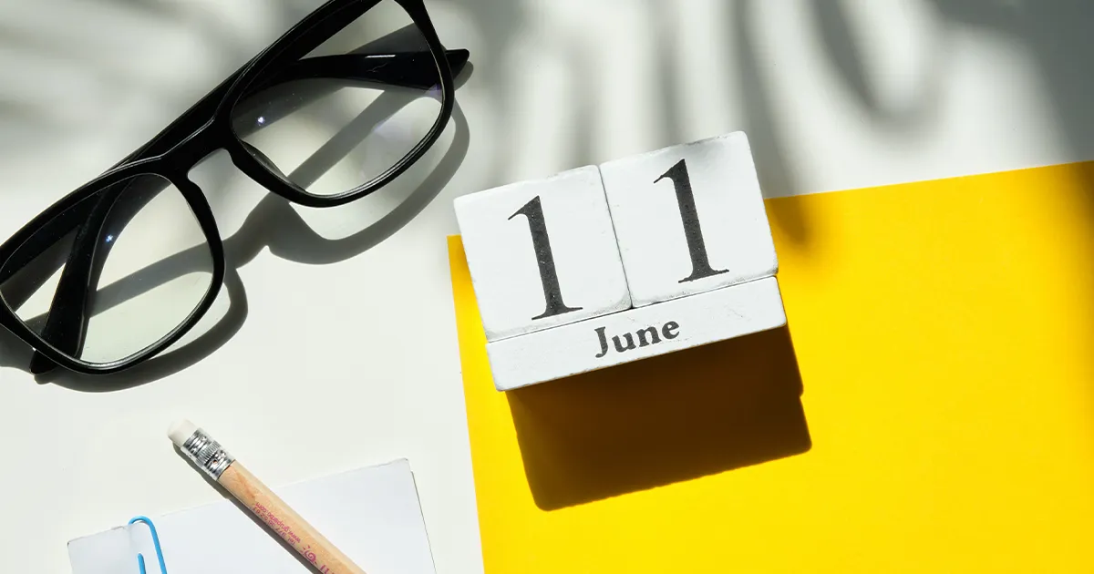 Ein Kalender auf einem Schreibtisch zeigt den 11. Juni an. Daneben liegen ein Notizblock und eine Brille.